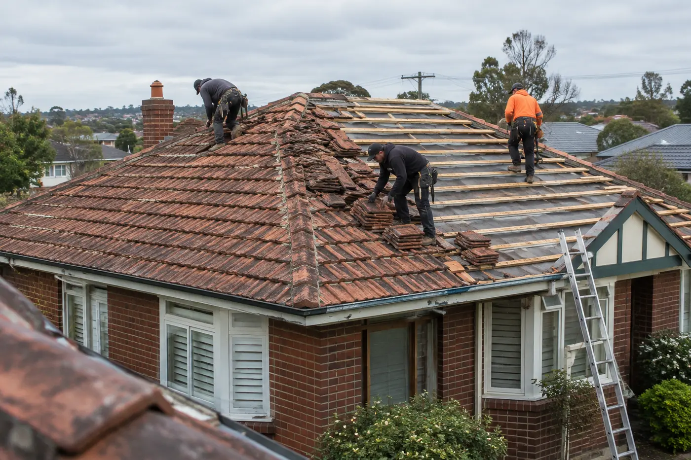 Old terracotta tiles being stripped from a brick bungalow roof in Melbourne's north, with new battens and sarking exposed
